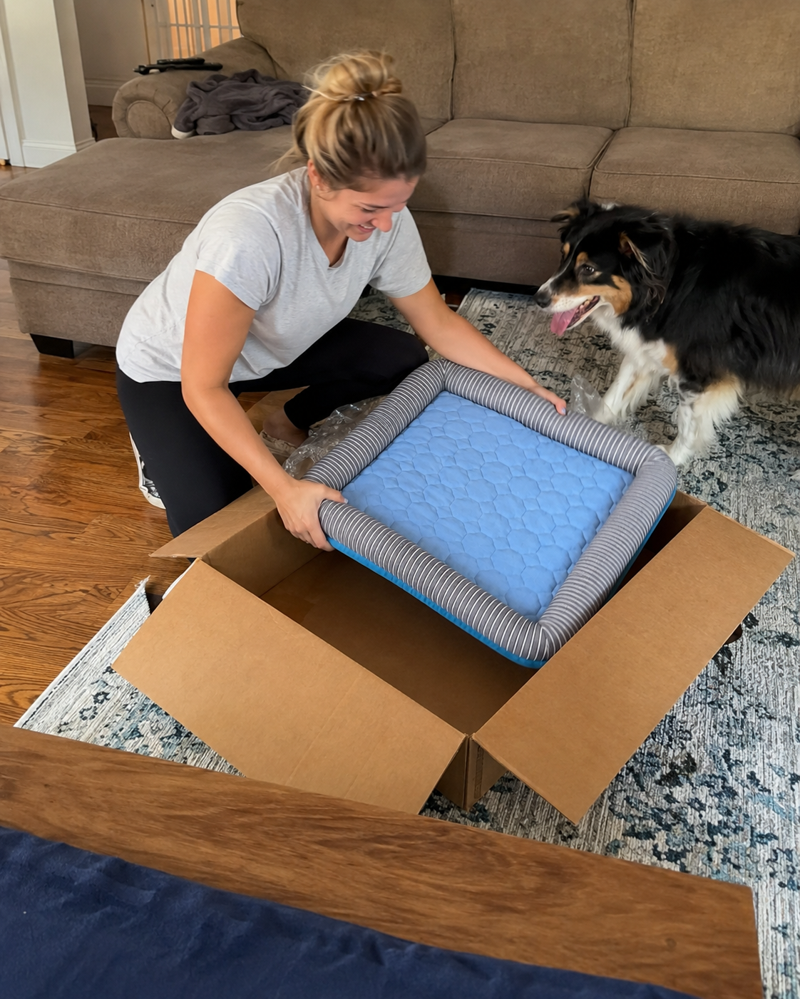 Customer unboxing a CanisCool cooling bed while her border collie watches